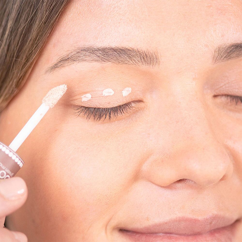 Gros plan d'une femme appliquant une base à paupières beige sur sa paupière avec un applicateur.