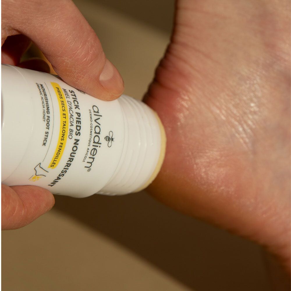 Gros plan: personne frottant le pied avec un stick. Inscription: ALVADIEM, STICK PIEDS NOURRISSANT.