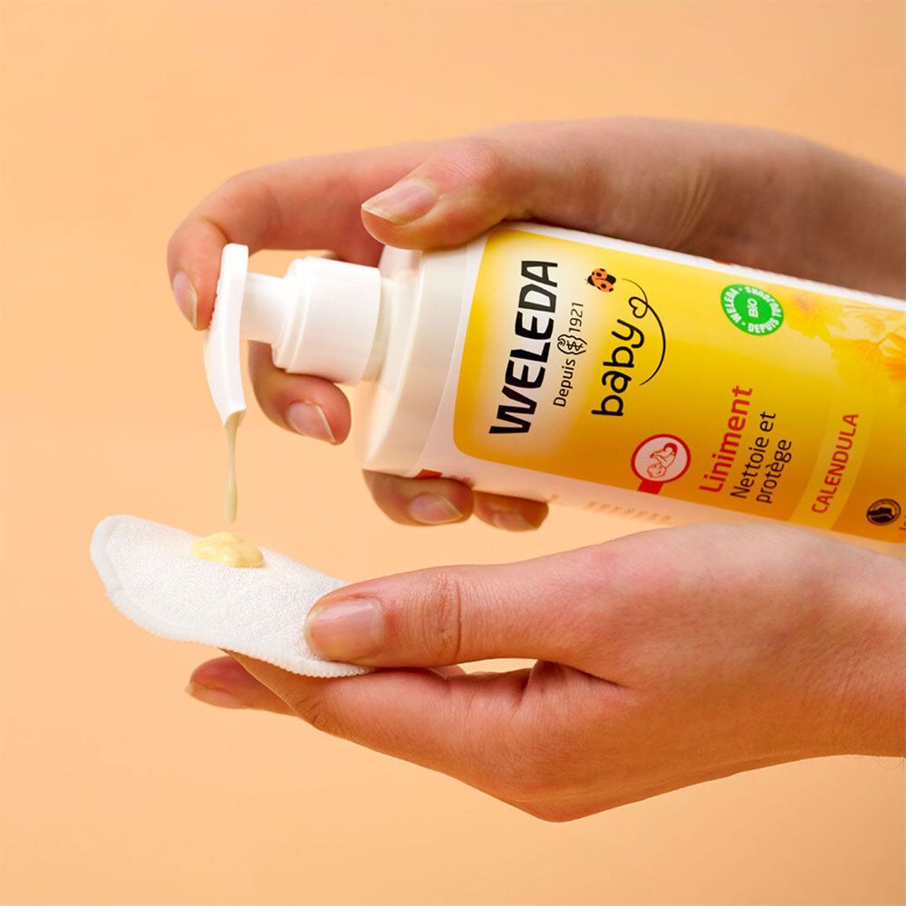 Mains tenant un flacon WELEDA Baby Liniment et versant du liquide sur un coton.