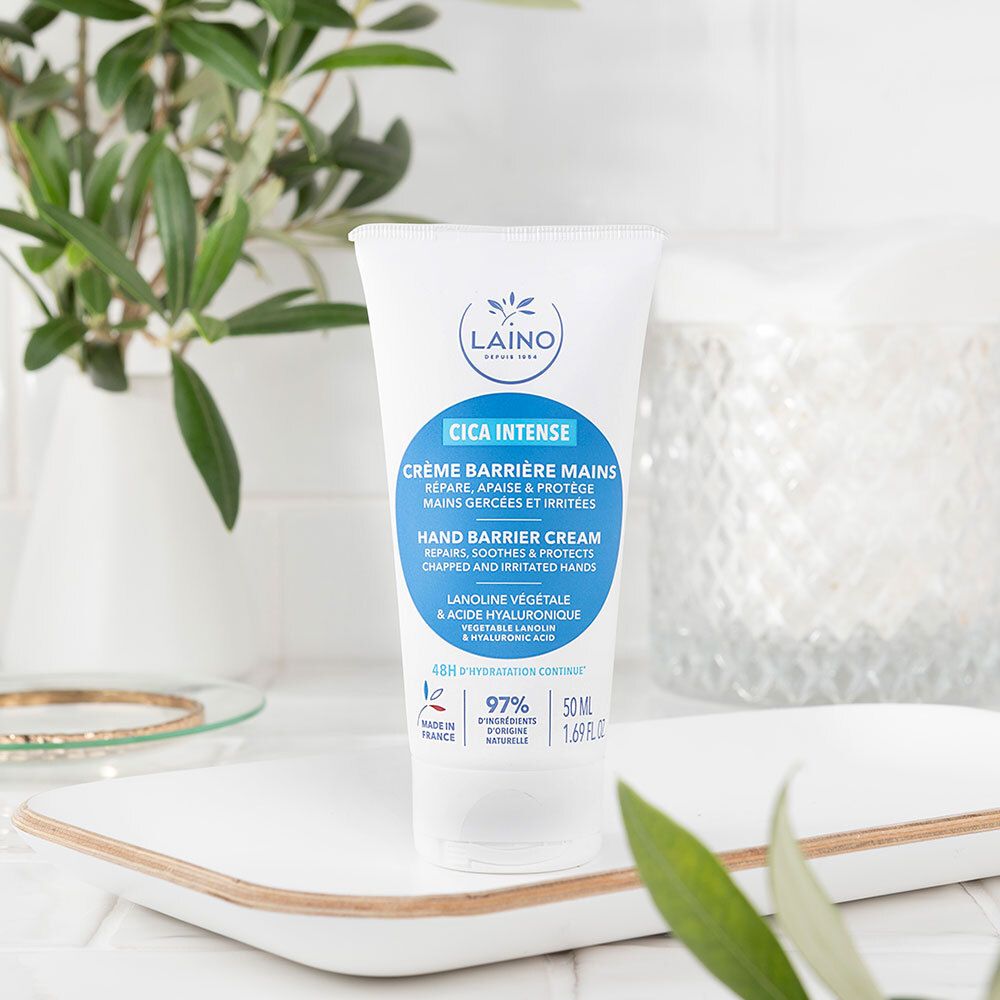Tube blanc sur plateau blanc. En arrière-plan: plantes et décoration. Texte: Cica Intense, Crème Barrière Mains.