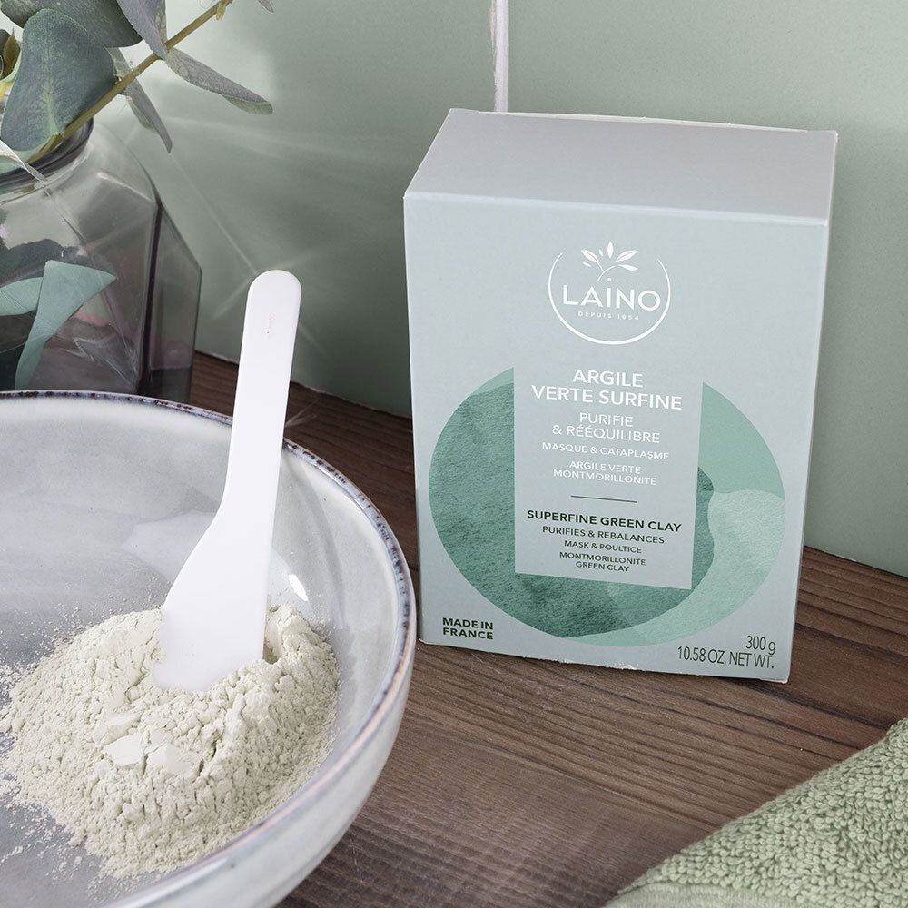Bol de poudre verte et spatule à côté d'une boîte vert clair avec logo LAINO et nom du produit : Argile Verte Surfine.