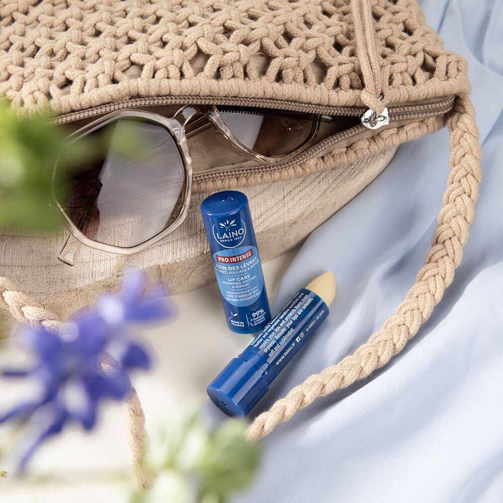 Deux sticks à lèvres bleus dans un sac beige avec des lunettes de soleil. Texte: LAINO, PRO INTENSE, LIP CARE.