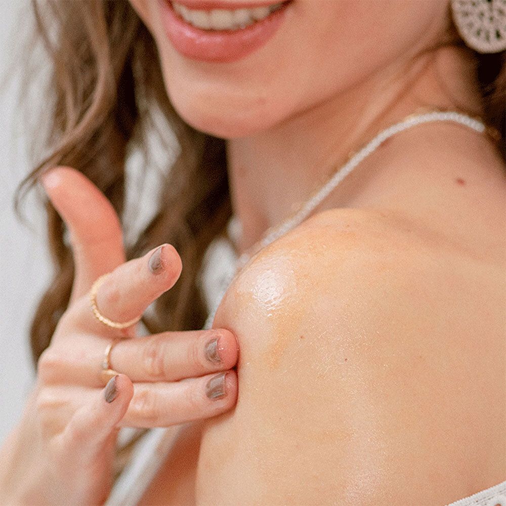 Personne appliquant de l'huile scintillante sur l'épaule. Huile dorée. Peau claire. Bagues sur la main.