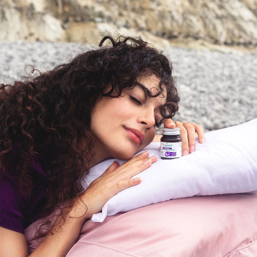 Femme allongée sur oreiller, tenant un flacon. Flacon brun avec étiquette produit. Environnement de sommeil.