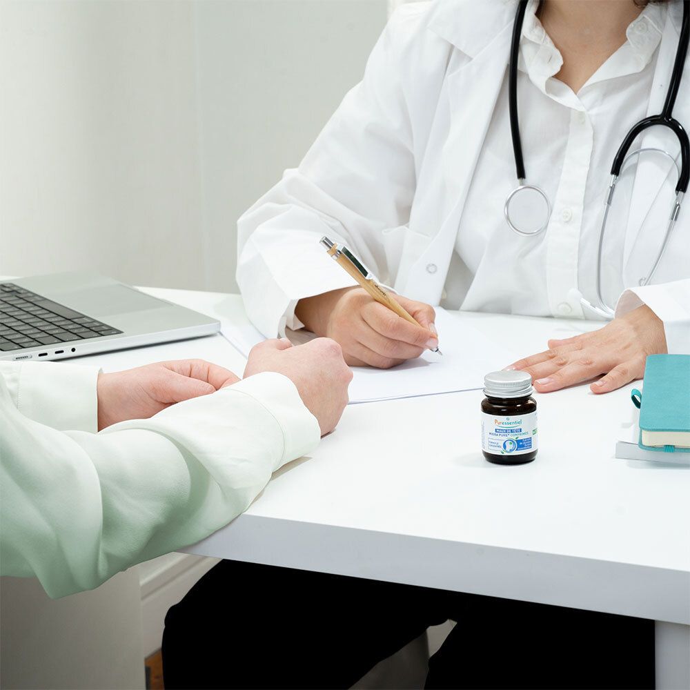 Médecin et patient à une table. Sur la table : flacon avec texte. Inscription : Maux de tête Migra Pure® Comprimés.