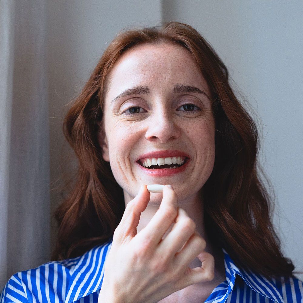 Femme avec un comprimé. Elle tient un comprimé entre ses doigts. Elle sourit.