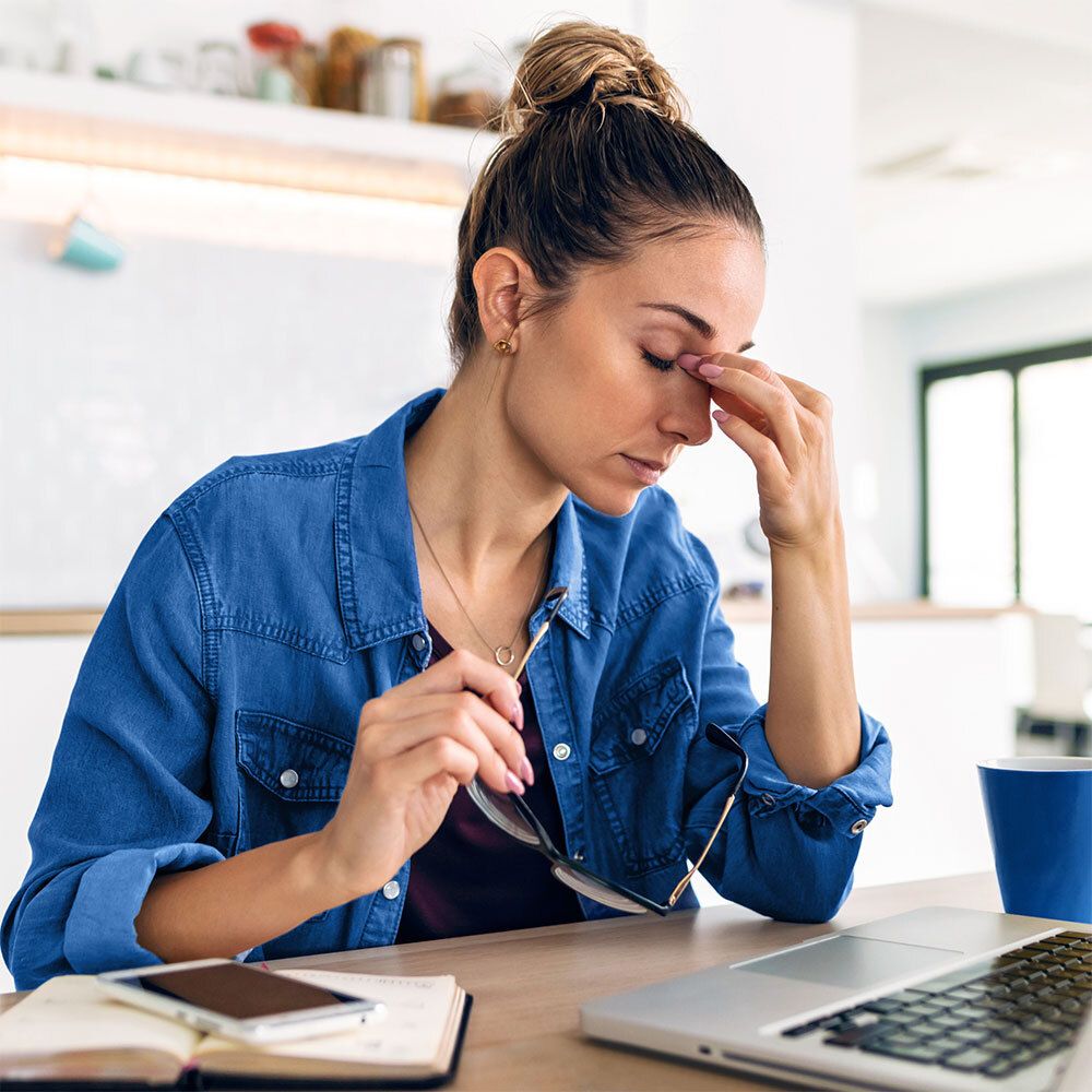 Femme avec ordinateur portable. Elle touche ses yeux. Lunettes et téléphone sur la table.