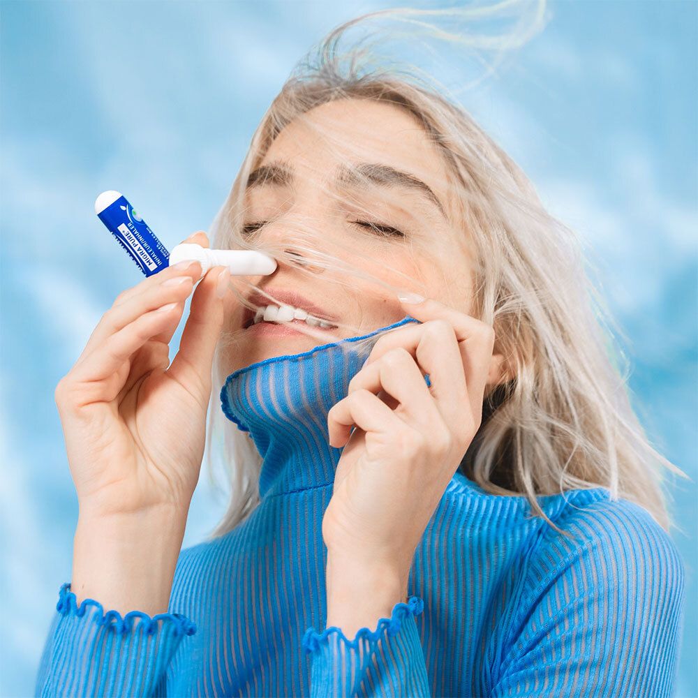 Femme avec inhalateur. Elle le tient près du nez. Fond bleu.
