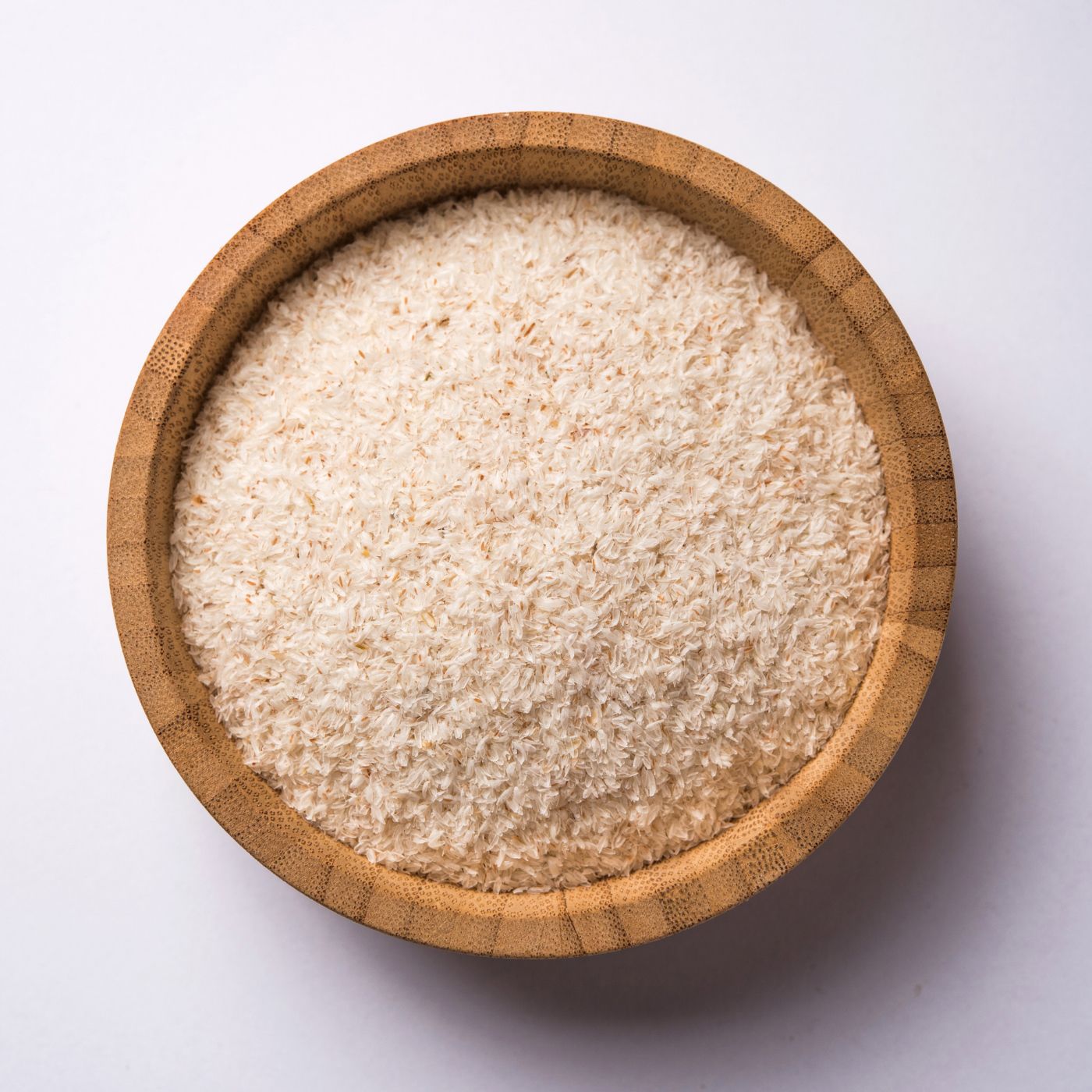 Bol en bois rempli de psyllium blond. Sur fond blanc. Vue de dessus.