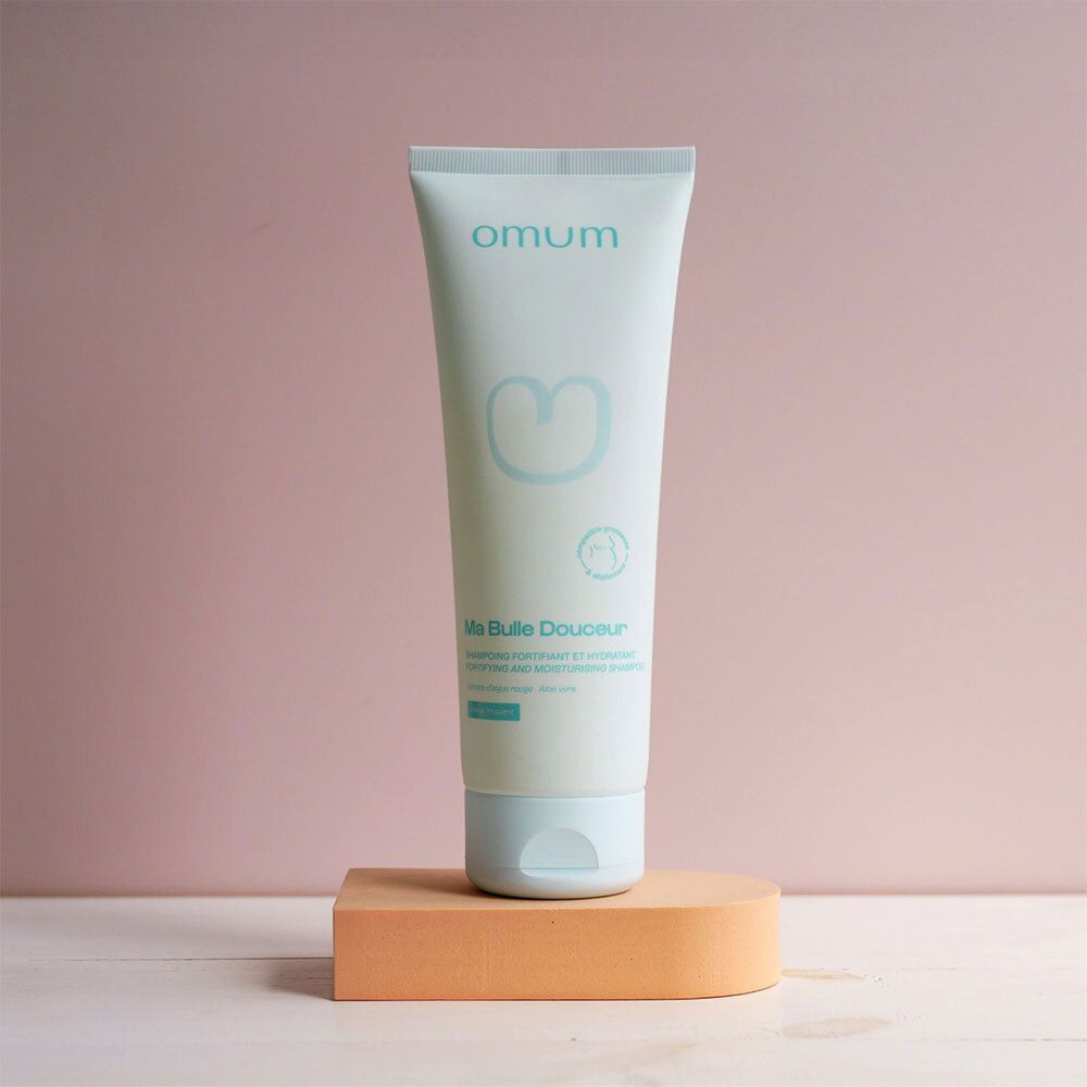 Tube Omum sur un socle orange devant un fond rose.