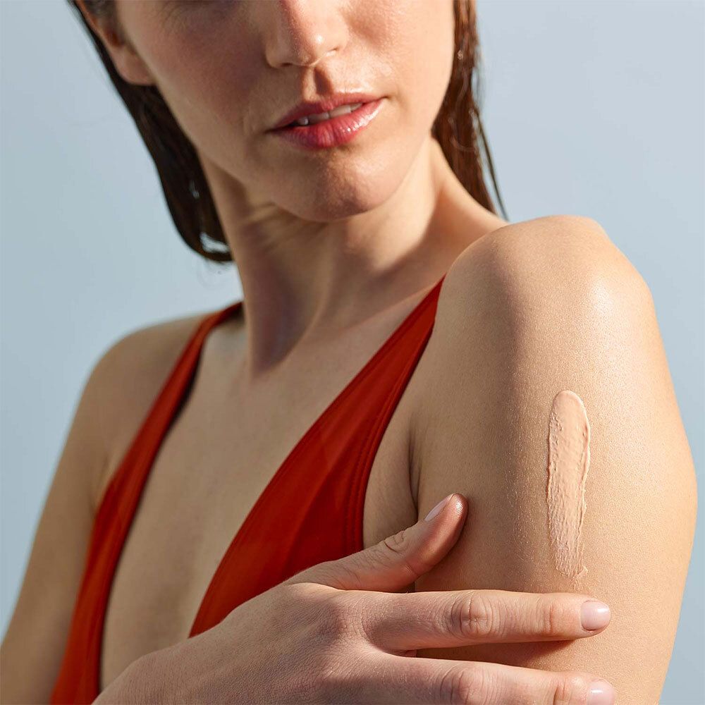 Personne appliquant de la crème solaire sur le bras. Texte: LABORATOIRES DE BIARRITZ, 50 SPF, Lait Solaire Invisible.