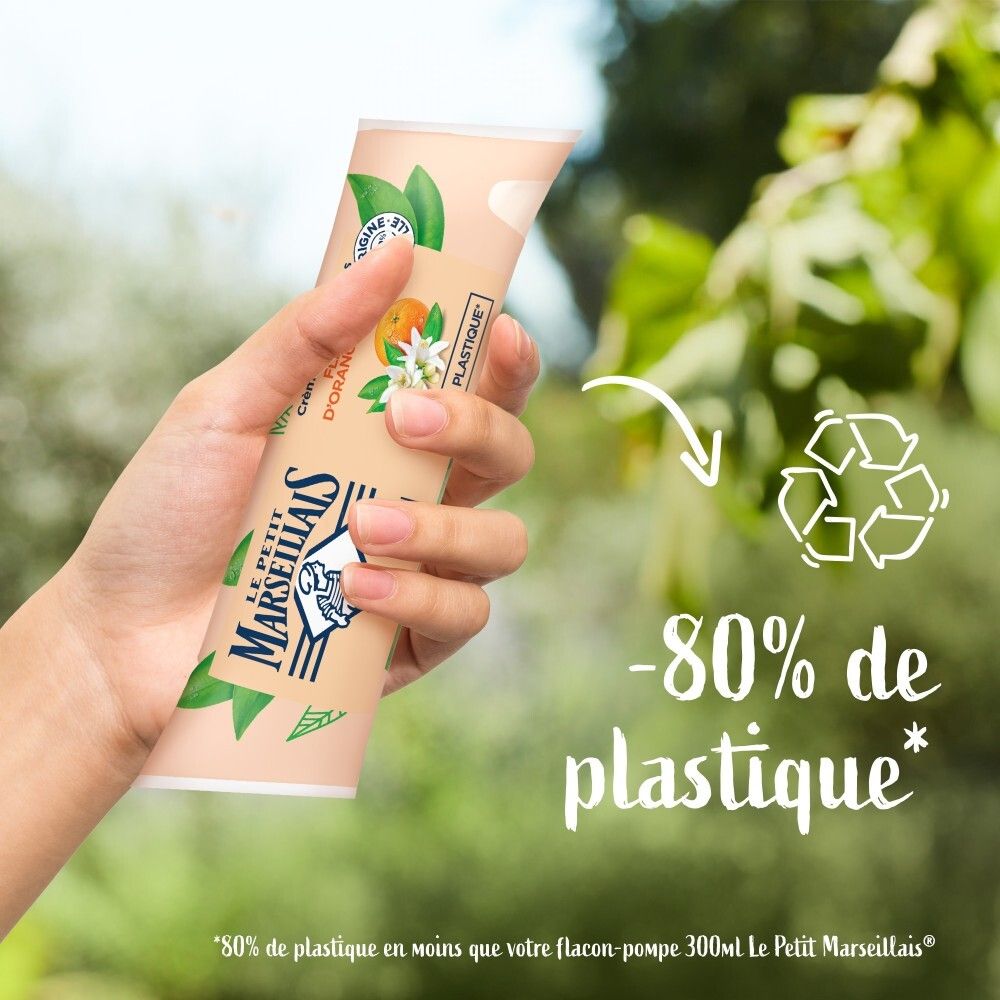 Main tenant la crème lavante Le Petit Marseillais Fleur d'Oranger Bio. Indication -80% de plastique.