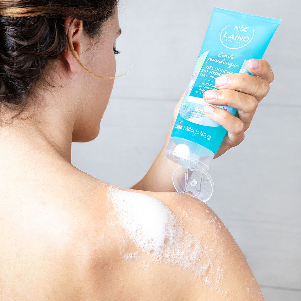 Personne se lave le dos avec un tube turquoise. Mousse sur la peau. Bouchon ouvert.