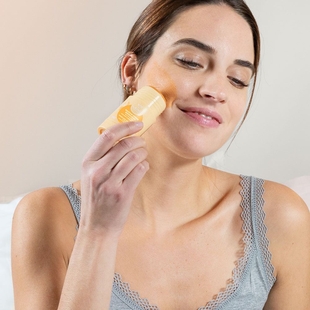 Femme appliquant un masque jaune sur son visage. Elle tient le masque.