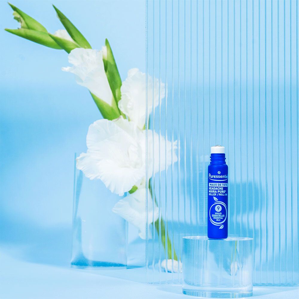 Roll-on bleu. Marque : Puressentiel. Texte : Maux de tête. Sur plaque de verre devant fleurs.