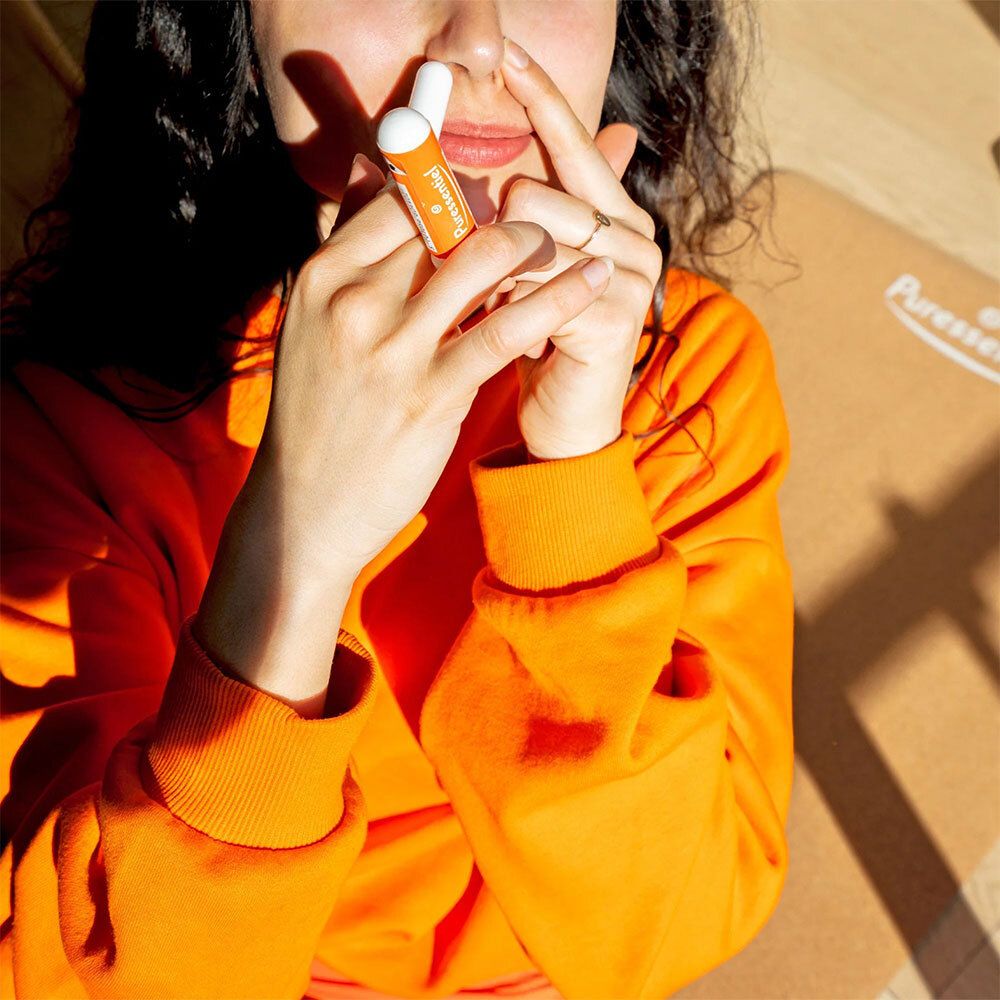 Une personne tient un inhalateur blanc et orange devant son nez. Elle porte un sweat-shirt orange.