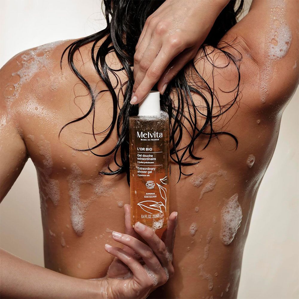 Personne avec Gel Douche Extraordinaire. Flacon avec texte: L'Or Bio, Gel Douche Extraordinaire.