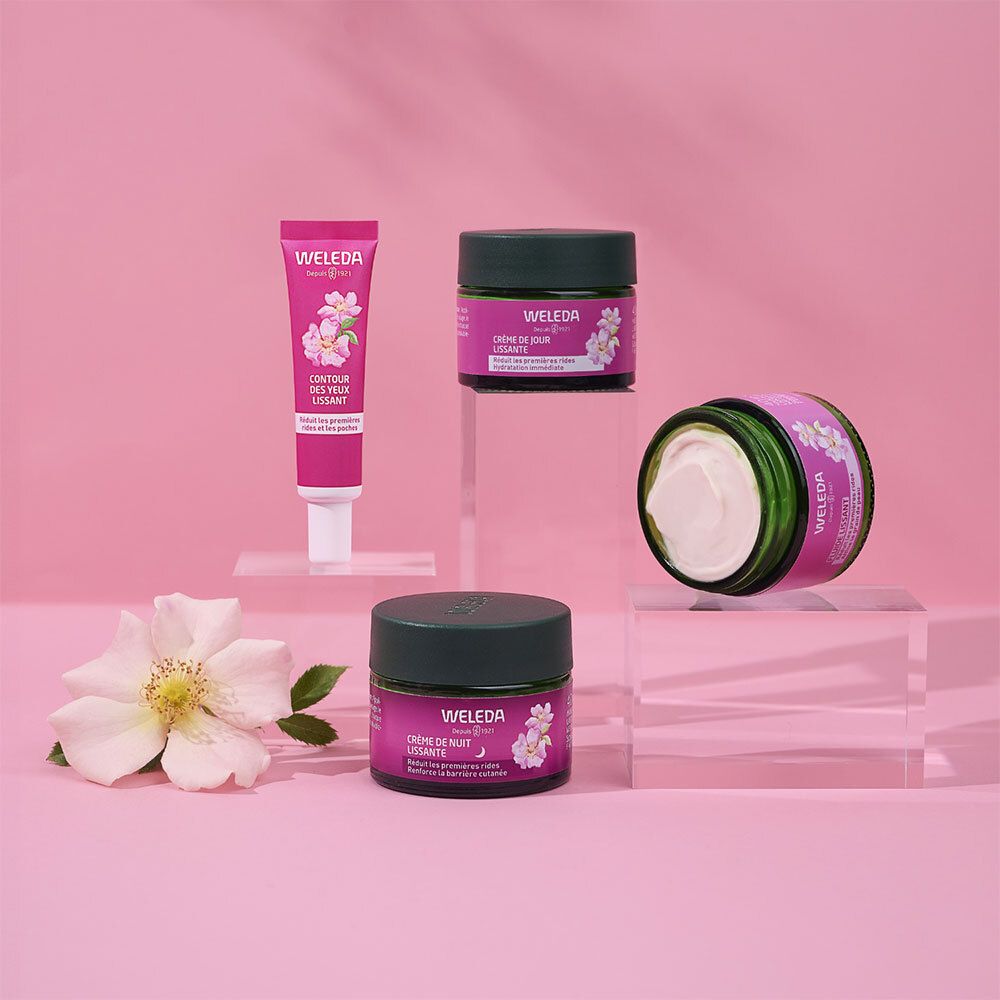 Produits Weleda : crème de nuit, crème de jour et tube de soin contour des yeux, disposés avec une rose.