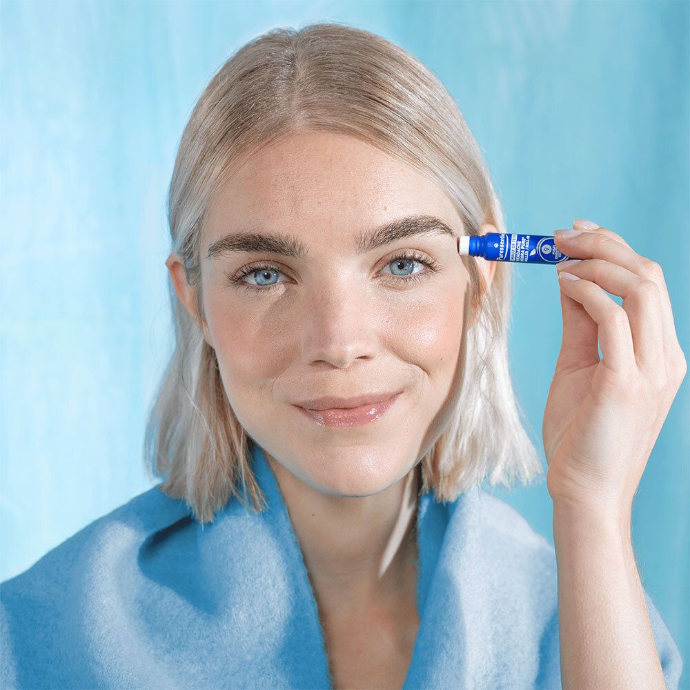 Femme tenant un roll-on bleu. Elle sourit. Fond bleu clair.