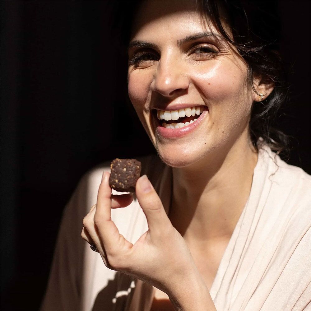 Femme tenant un petit snack brun. Elle sourit.