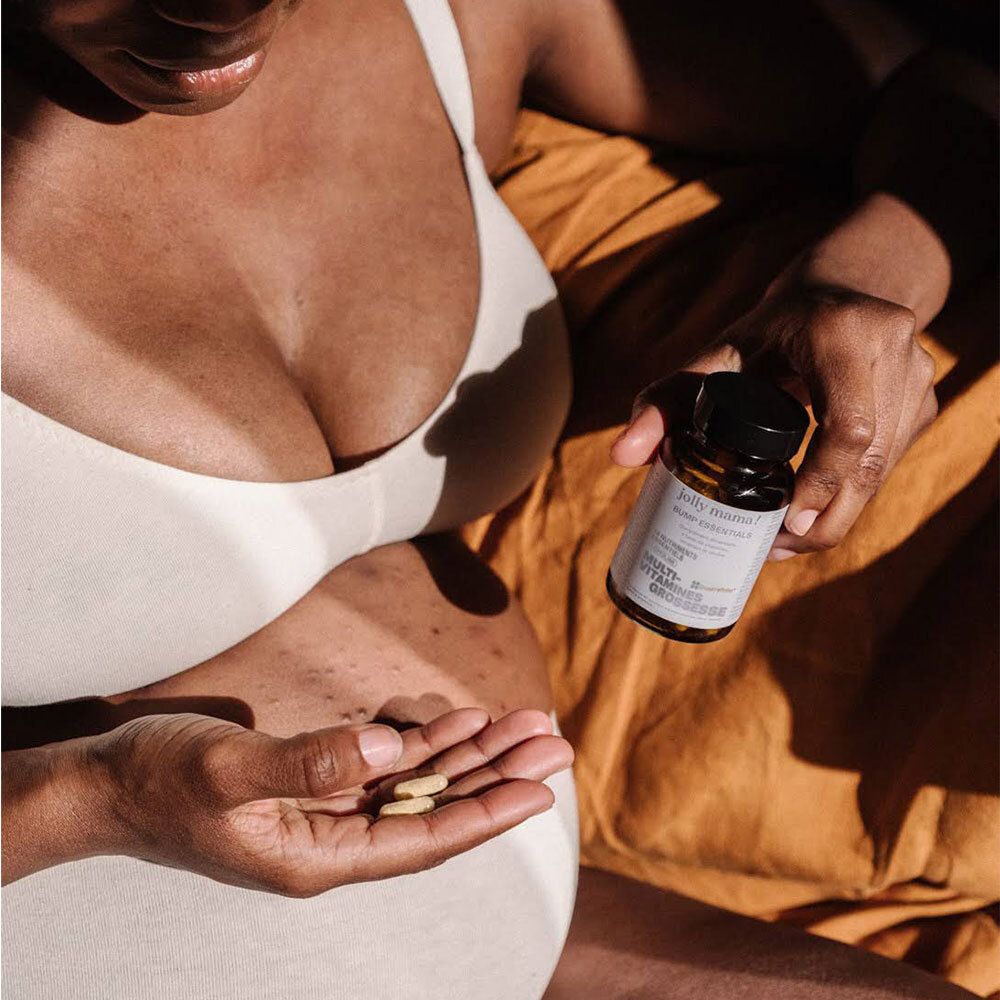 Femme enceinte tenant un flacon et des gélules. Flacon avec étiquette : Jolly Mama Bump Essentials.