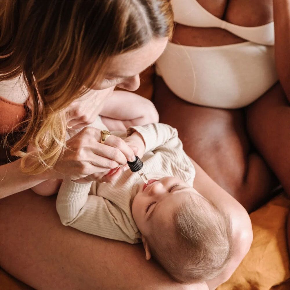Une personne verse du liquide d'une pipette dans la bouche d'un bébé. Le bébé est sur les genoux d'une autre personne.