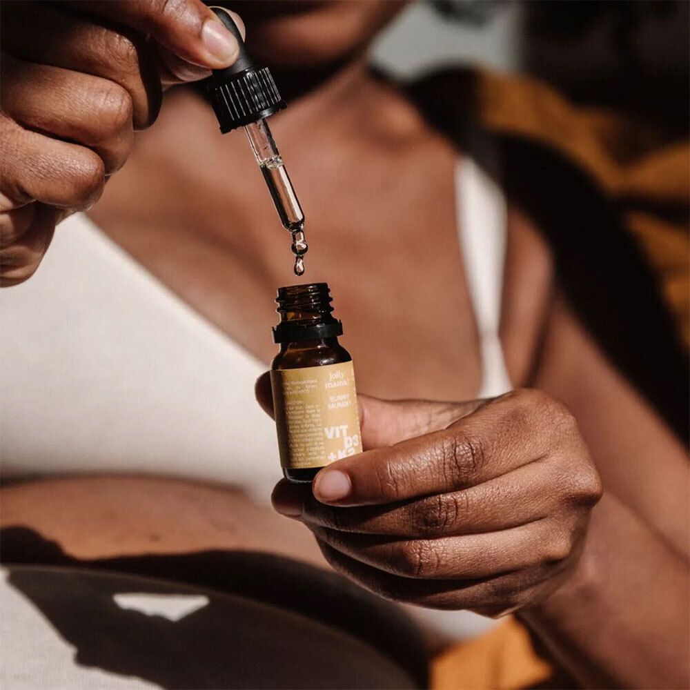 Personne tenant une bouteille brune avec compte-gouttes. Des gouttes tombent dans la bouteille. Bouteille avec une étiquette jaune.