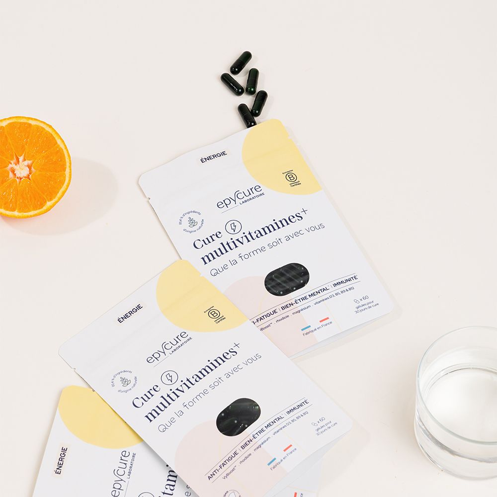 Plusieurs sachets Cure multivitamines+. Inscription: epycure, certification B. Orange et verre d'eau à côté.