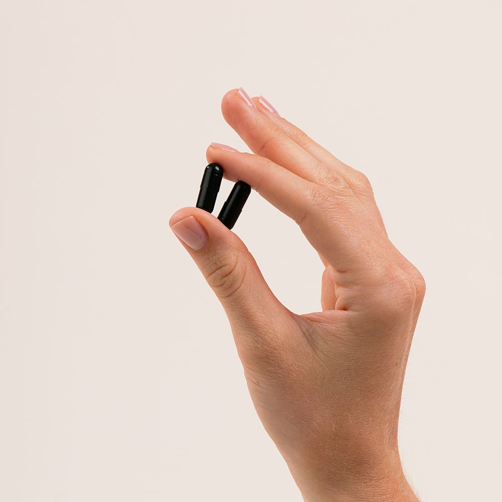 Main tenant deux gélules. Gélules vert foncé, forme allongée.