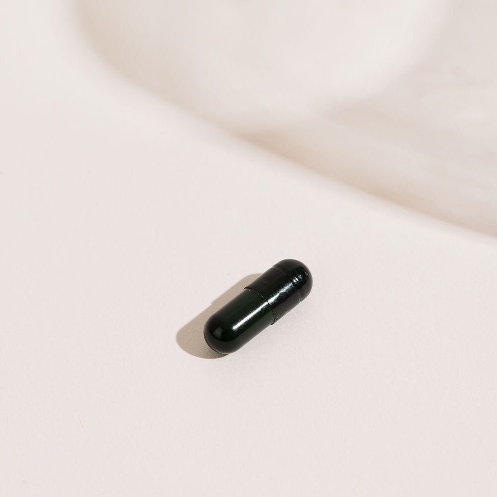 Une gélule vert foncé sur fond clair.