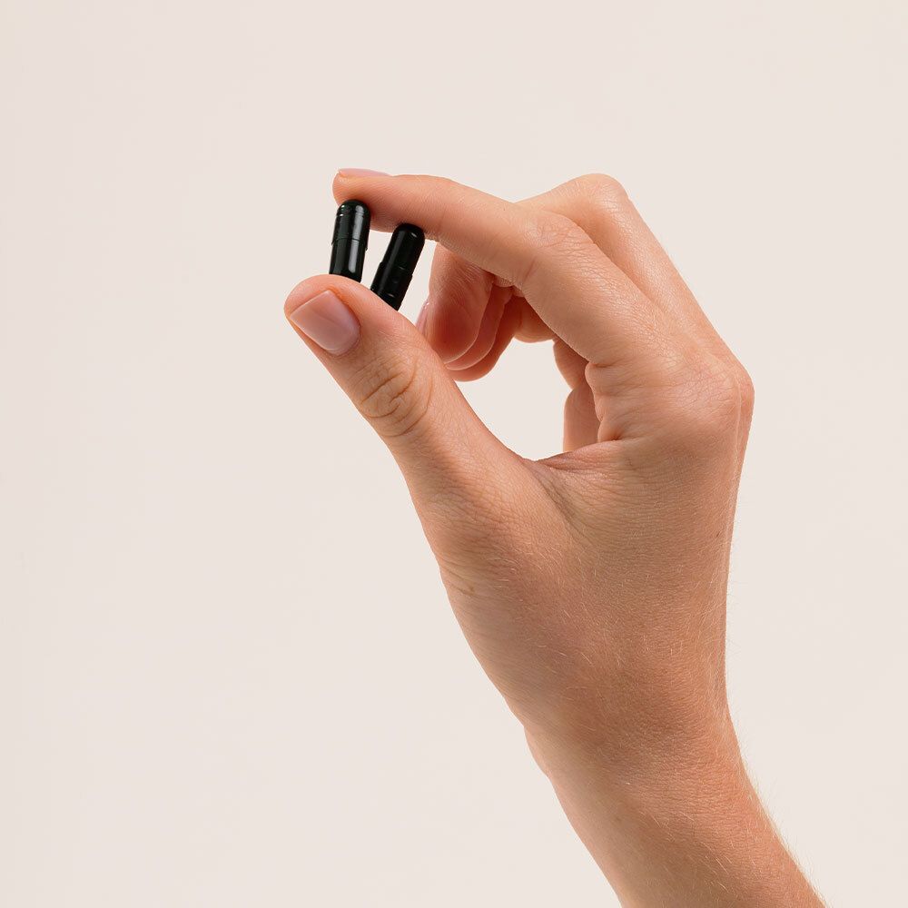 Main tenant deux gélules vert foncé.