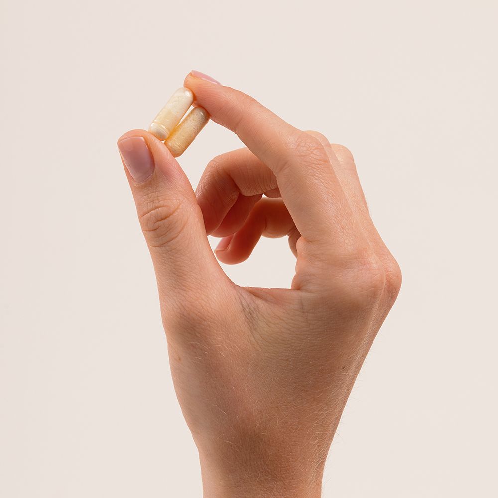 Main tenant deux gélules. Les gélules sont brun clair. Fond clair.