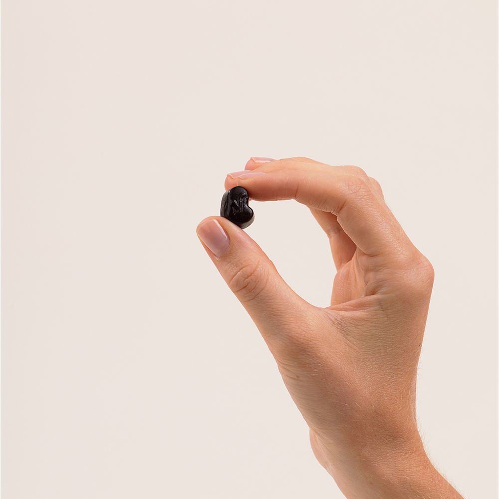 Main tenant un gummy noir en forme de cœur. Fond blanc.