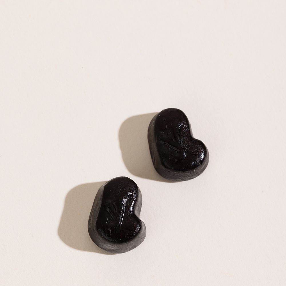 Deux gummies noirs en forme de cœur sur fond blanc.