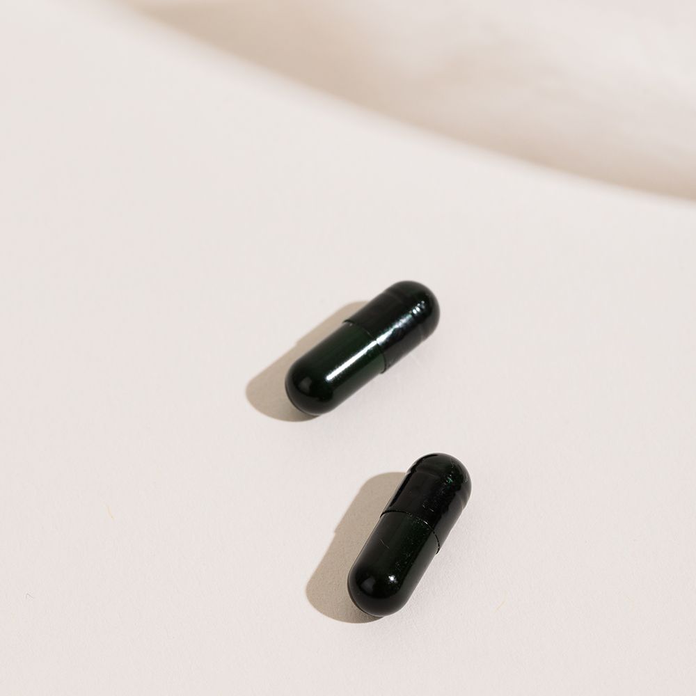 Deux gélules foncées sur fond blanc. Les gélules sont oblongues et brillantes.