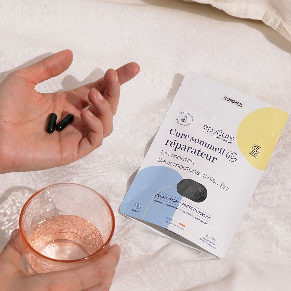 Emballage, gélules et verre sur linge de lit. Inscription: Cure sommeil réparateur. Marque: epycure. Emballage jaune et blanc.
