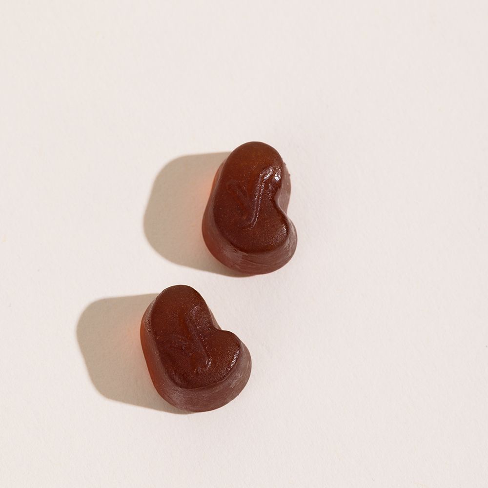 Deux gummies marron sur fond blanc. Forme: haricots.