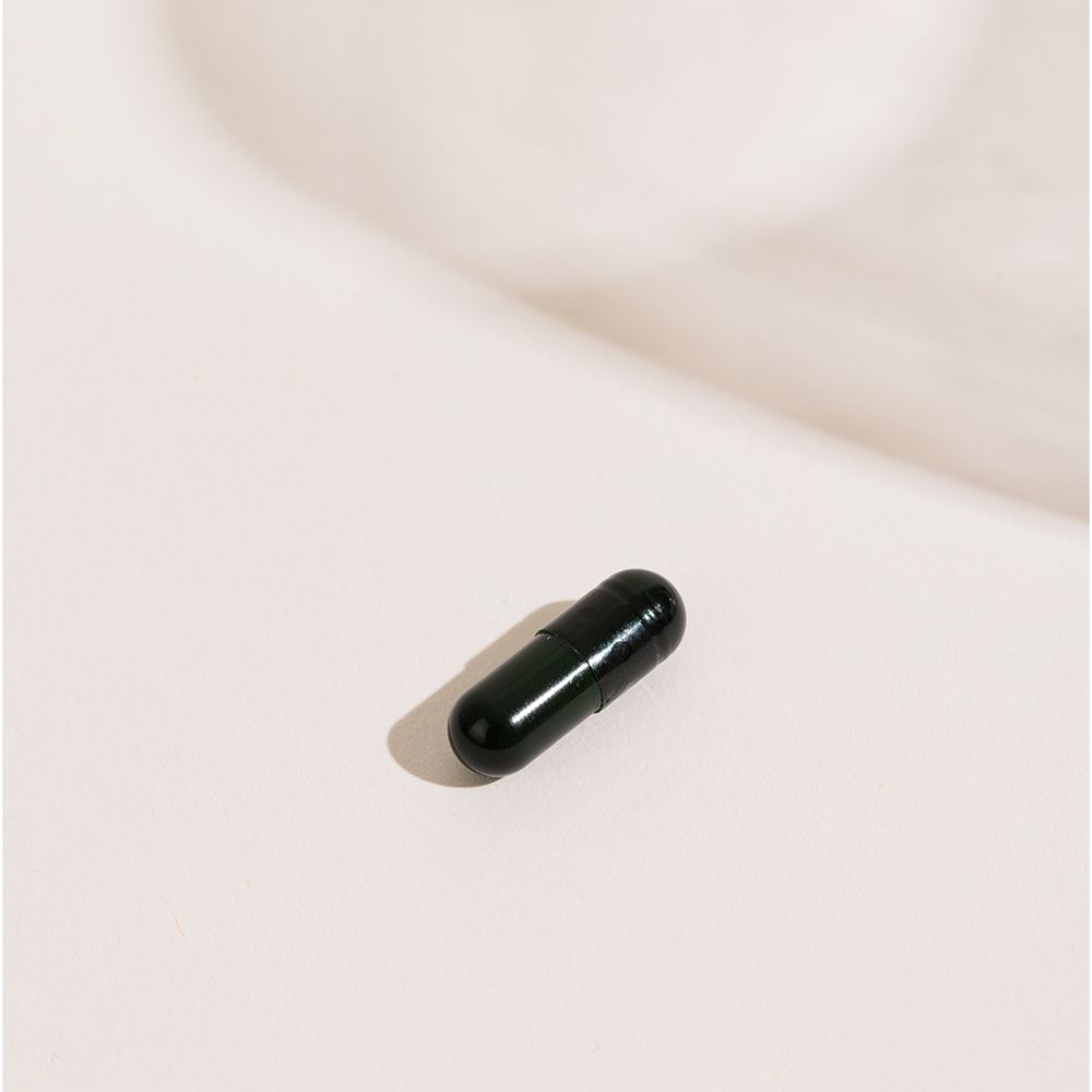 Gélule unique sur fond blanc. Forme oblongue vert foncé.