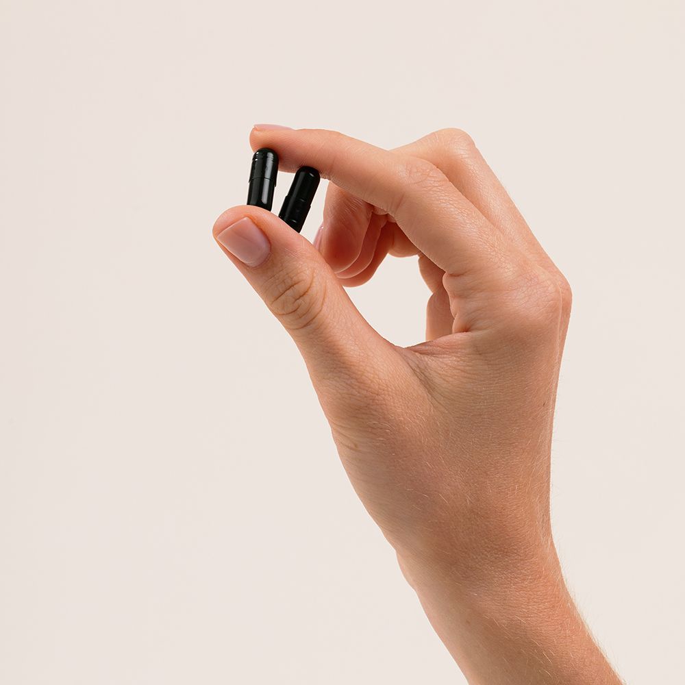 Main tenant deux gélules. Forme oblongue vert foncé.