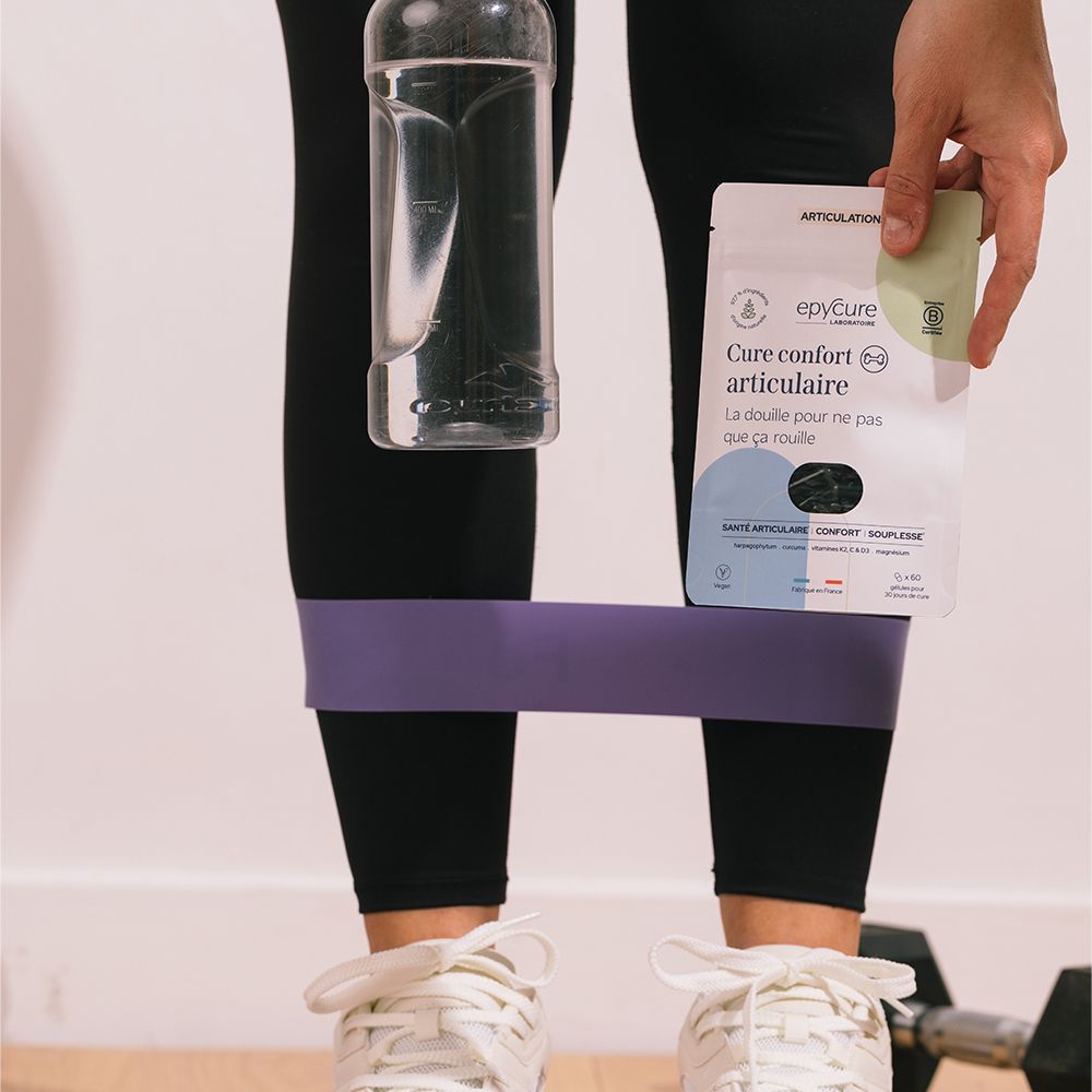Personne tenant l'emballage du produit et une bouteille d'eau. Bande de gymnastique autour des jambes.
