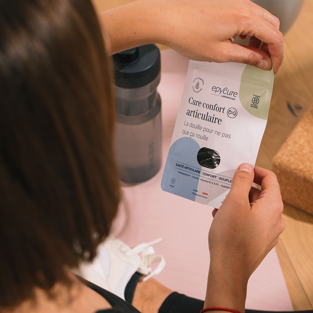 Personne tenant l'emballage du produit. Sur un tapis d'entraînement, à côté d'une bouteille d'eau.
