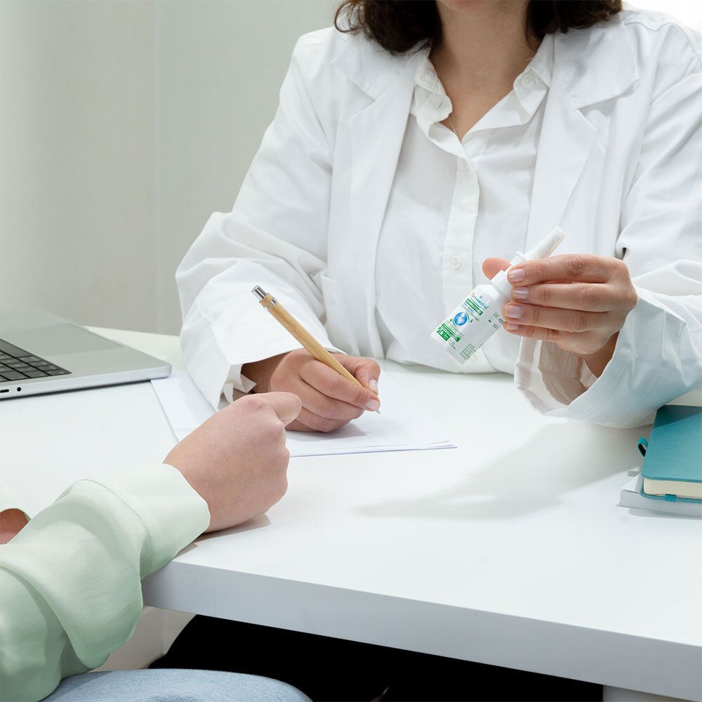 Médecin et patient. Le médecin tient un spray nasal. Notes et ordinateur portable sur la table.