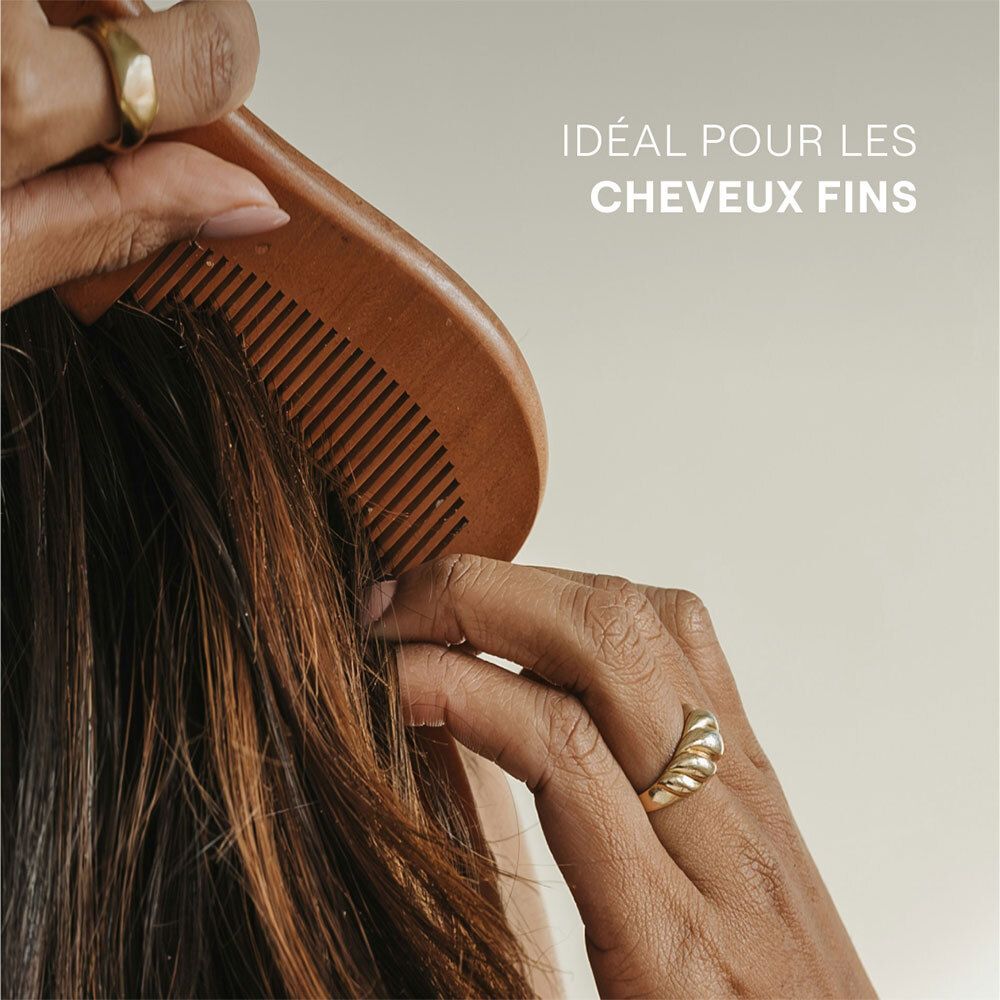 Main peignant les cheveux fins avec un peigne en bois. Texte: Idéal pour les cheveux fins.