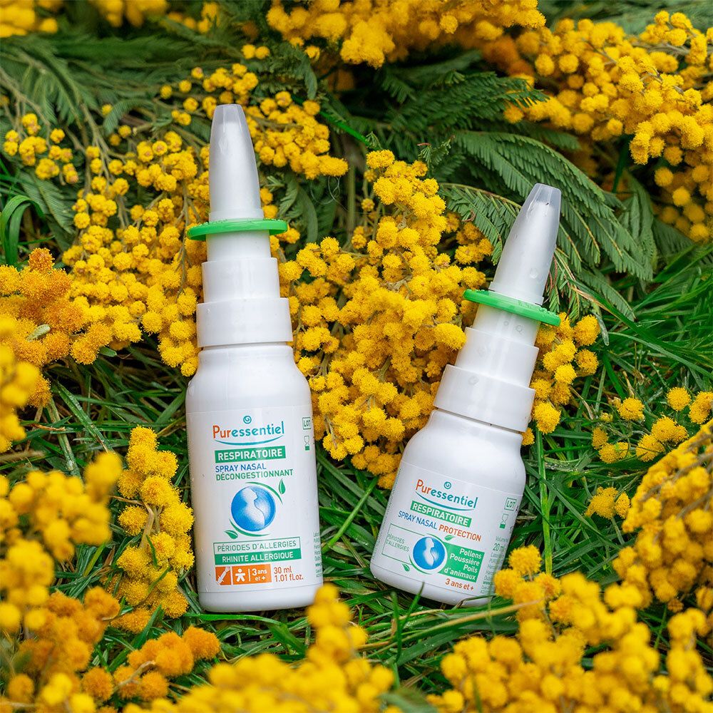 Deux flacons spray nasal Puressentiel avec embout, parmi des fleurs jaunes.