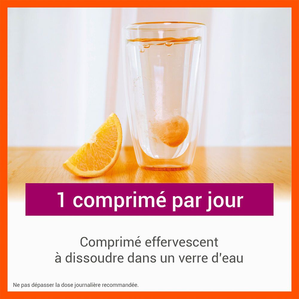 Comprimé effervescent COOPER Vitascorbol Energie se dissolvant dans un verre d'eau, quartier d'orange à côté.