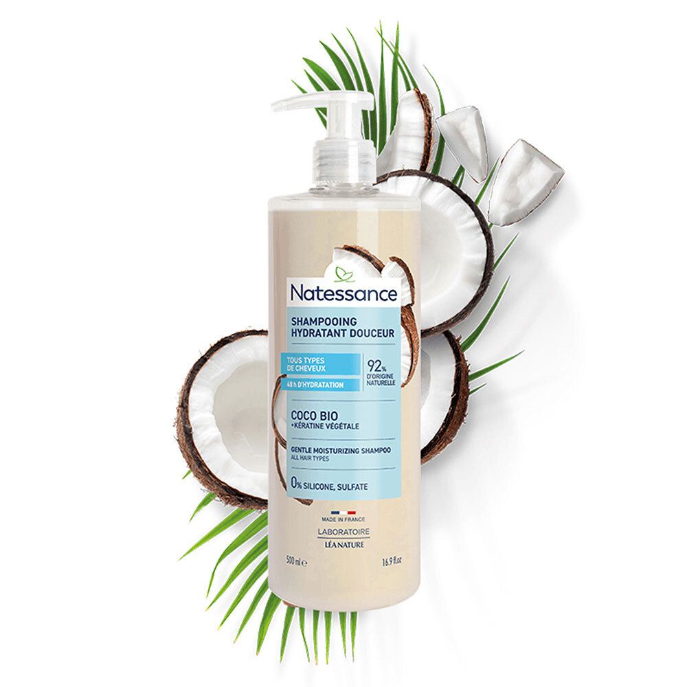 Flacon de Shampooing Hydratant Douceur Coco Natessance avec pompe, entouré de noix de coco et feuilles. Inscriptions : Coco Bio, 92% d'origine naturelle.