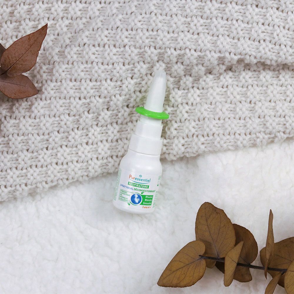 Spray nasal sur un tissu en maille crème. Des feuilles brunes entourent le produit.