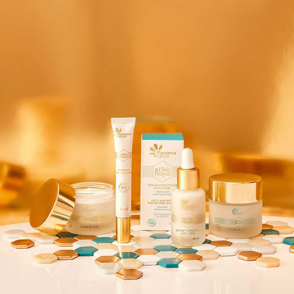 Plusieurs produits cosmétiques, dont un pot de crème, un sérum, une crème pour les yeux. Tons dorés et bleus. Inscription: Elixir Royal.