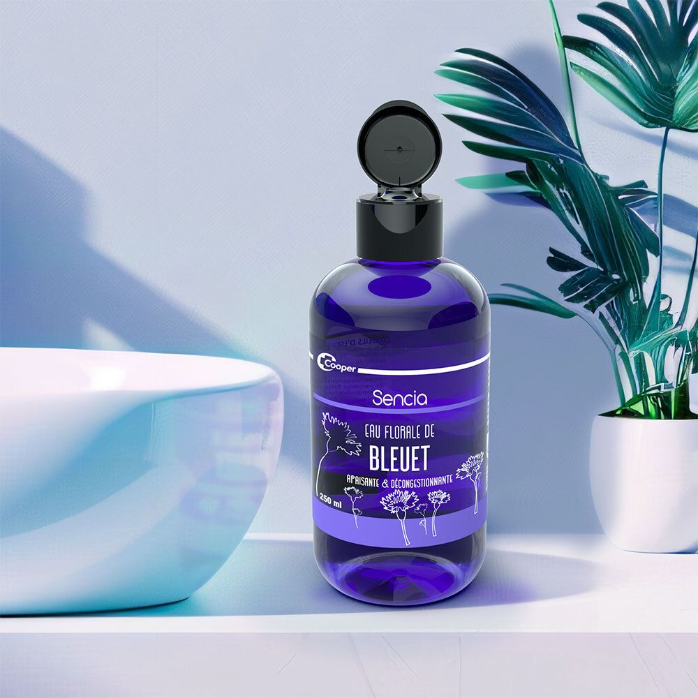 Flacon bleu avec bouchon noir. Inscription: Sencia Eau Florale de Bleuet. Marque: Cooper. Dans une salle de bain.
