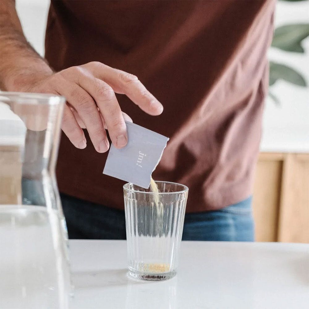 Une personne verse de la poudre d'un sachet dans un verre. Le sachet porte l'inscription "jm!".